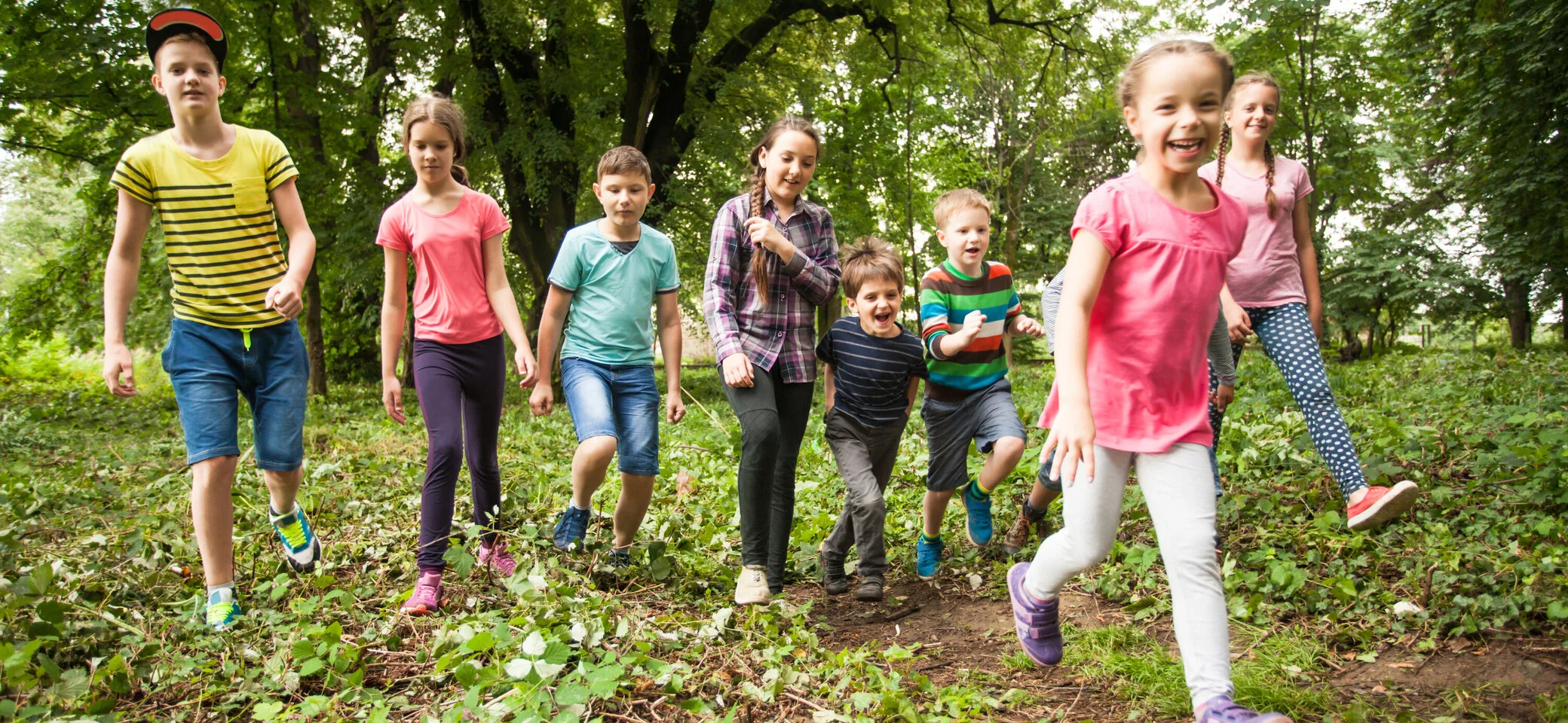 Viele Kinder wandern lachend durch ein Waldgebiet | © Oksix / Adobe Stock